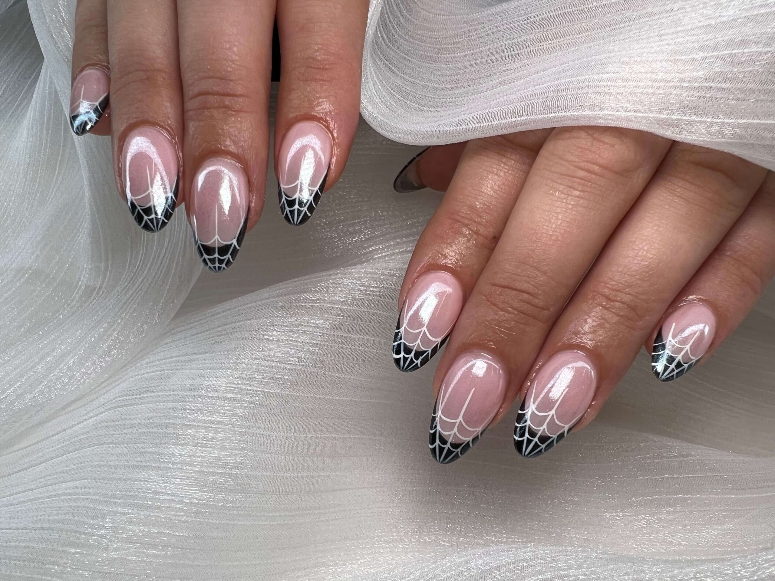 Almond-shaped fall nails with black and white spiderweb tip design.