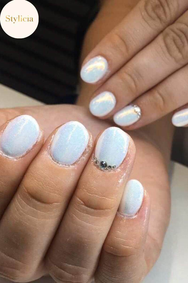 Iridescent short nails with white shimmer polish and crystal accents – elegant manicure design.