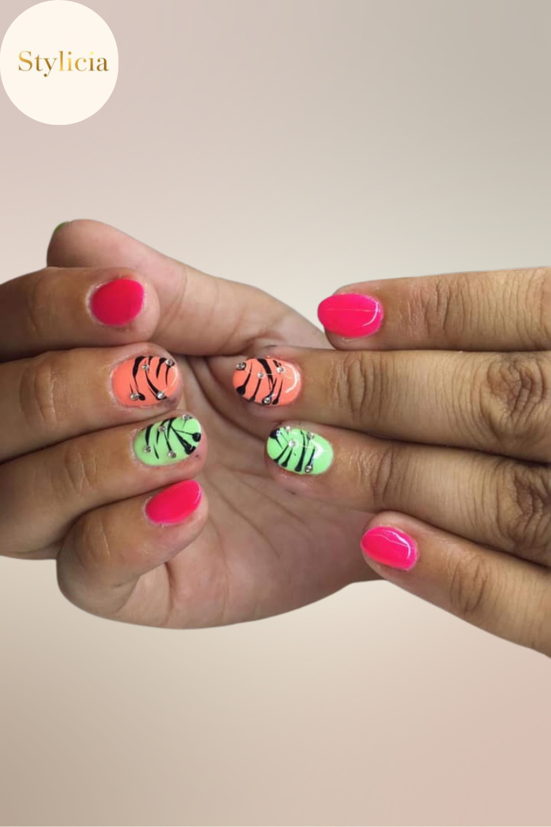 Vibrant short nails with neon pink, orange, and green polish featuring black zebra stripes and rhinestone accents.