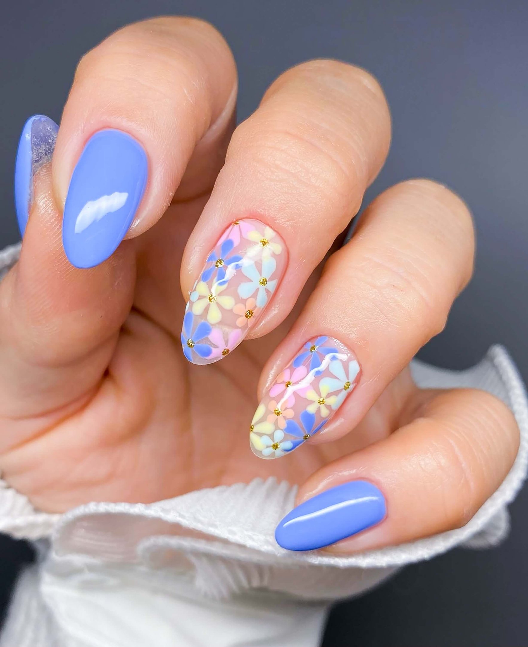Summer nail trend with pastel floral nail art in blue, pink, and yellow tones on almond-shaped nails, featuring delicate flower details and glossy finish.