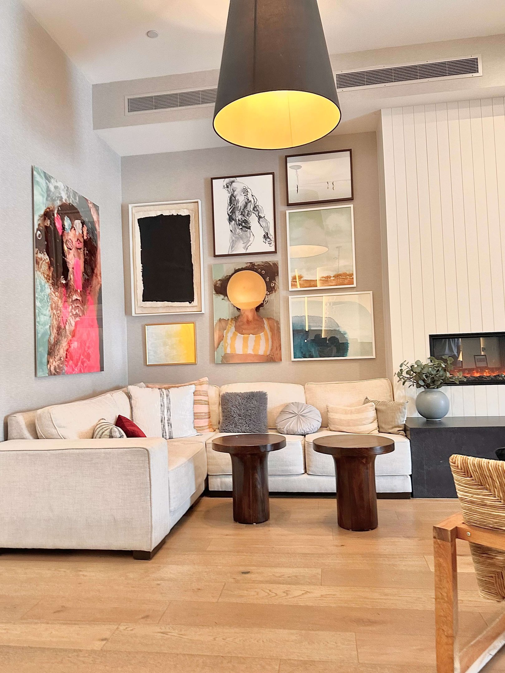 Modern living room with a neutral sectional sofa, cosy pillows, wooden coffee tables and a gallery wall of eclectic art – stylish home decorating ideas for a personalised space.