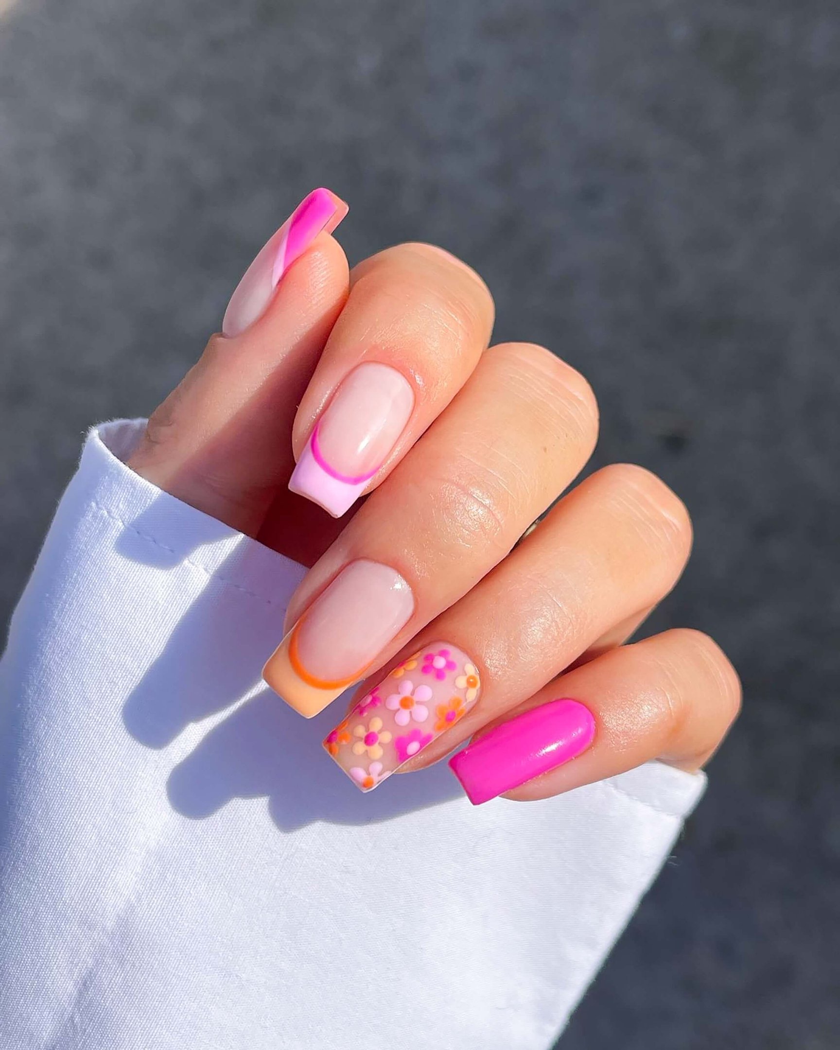 Summer nail trend with square-shaped nails featuring neon pink polish, colorful French tips in orange and pink, and daisy floral nail art accent.