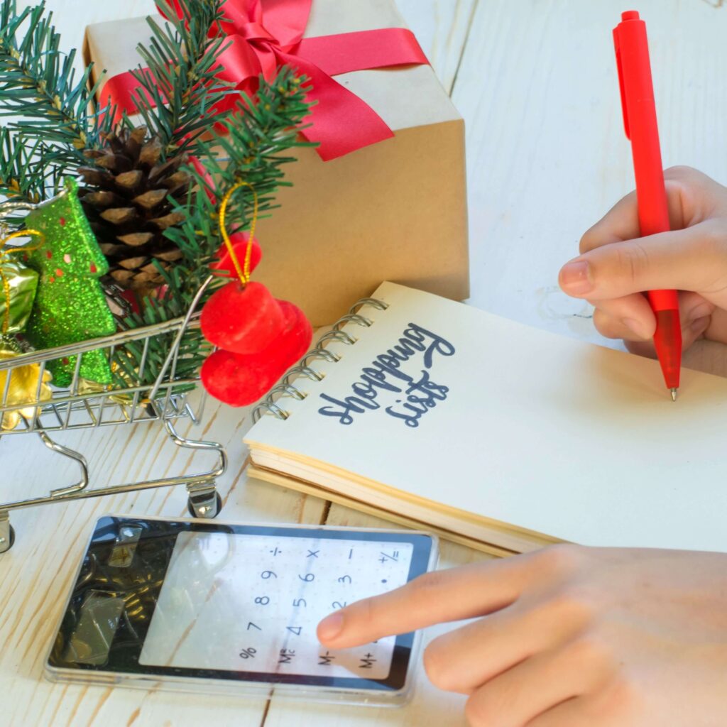 Woman writing a Christmas budget list beside wrapped gifts and holiday decorations — a cozy reminder to get ready for Christmas in November with simple, stress-free spending plans.