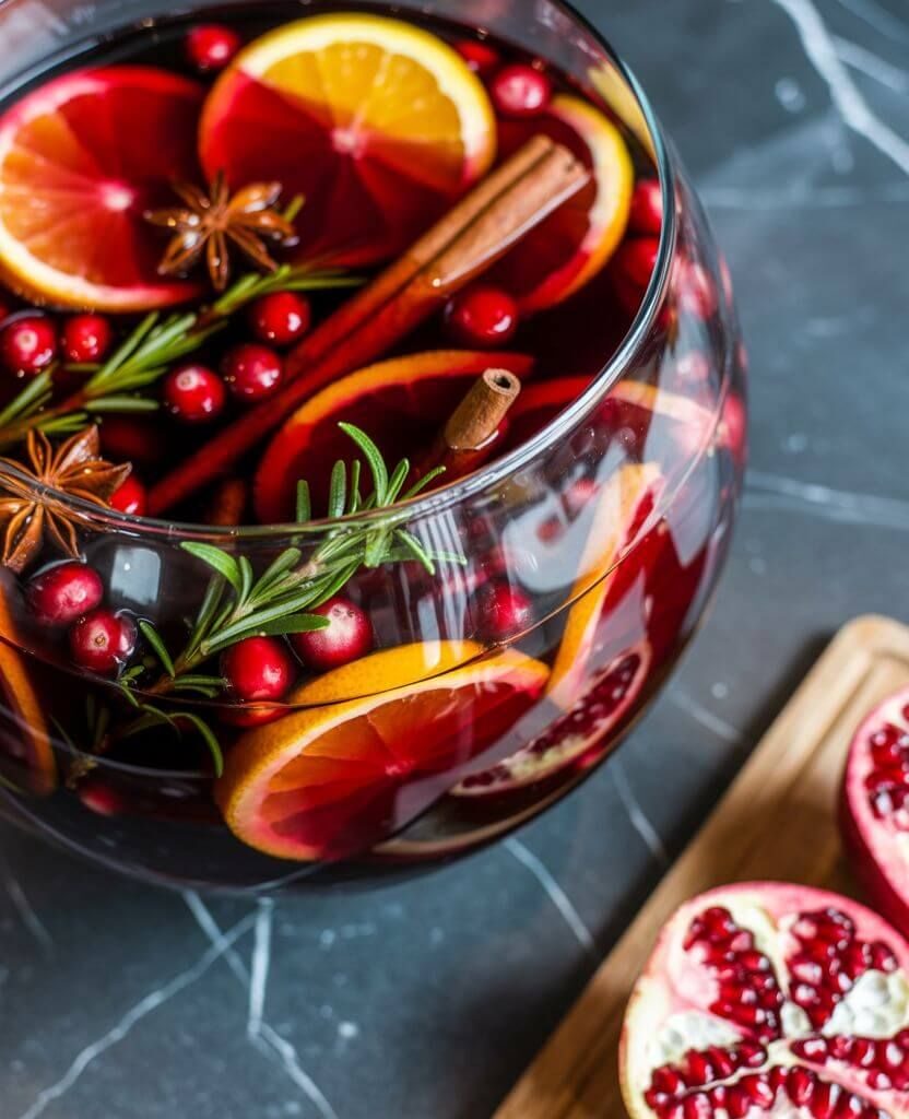Glass bowl of easy non-alcoholic autumn punch with orange slices, cranberries, pomegranate, rosemary, and cinnamon sticks – the perfect festive fall punch recipe.