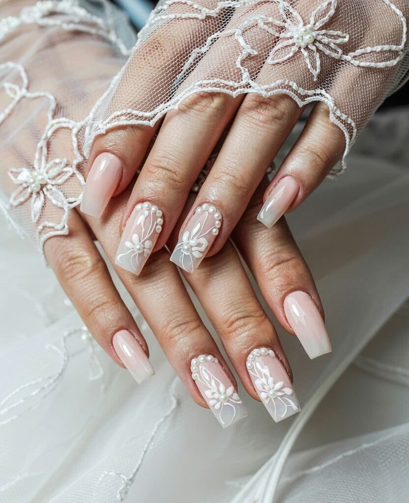 Close-up of elegant wedding nails with a soft pink ombré base, white floral designs, and pearl accents, perfect for a bridal manicure.