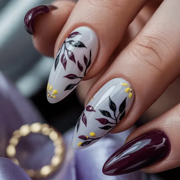 Almond burgundy fall nails — deep wine solid accents with dark botanical leaf design and small yellow details on pale base — one of many fall nail ideas for autumn