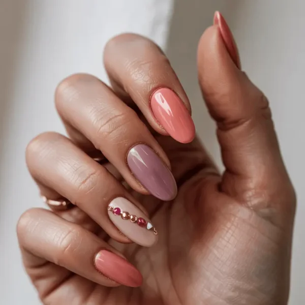 Almond fall nails — peachy coral, dusty rose, and light blush tones with gold and pink bead chain accent detail