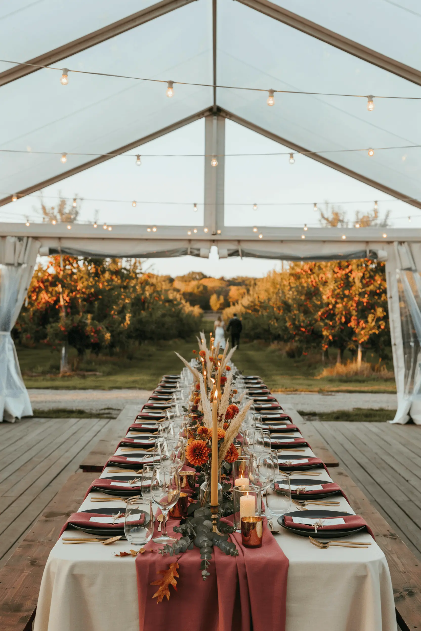 Fall outdoor wedding tent with sidewalls down, string lights and candles running the length of the tables