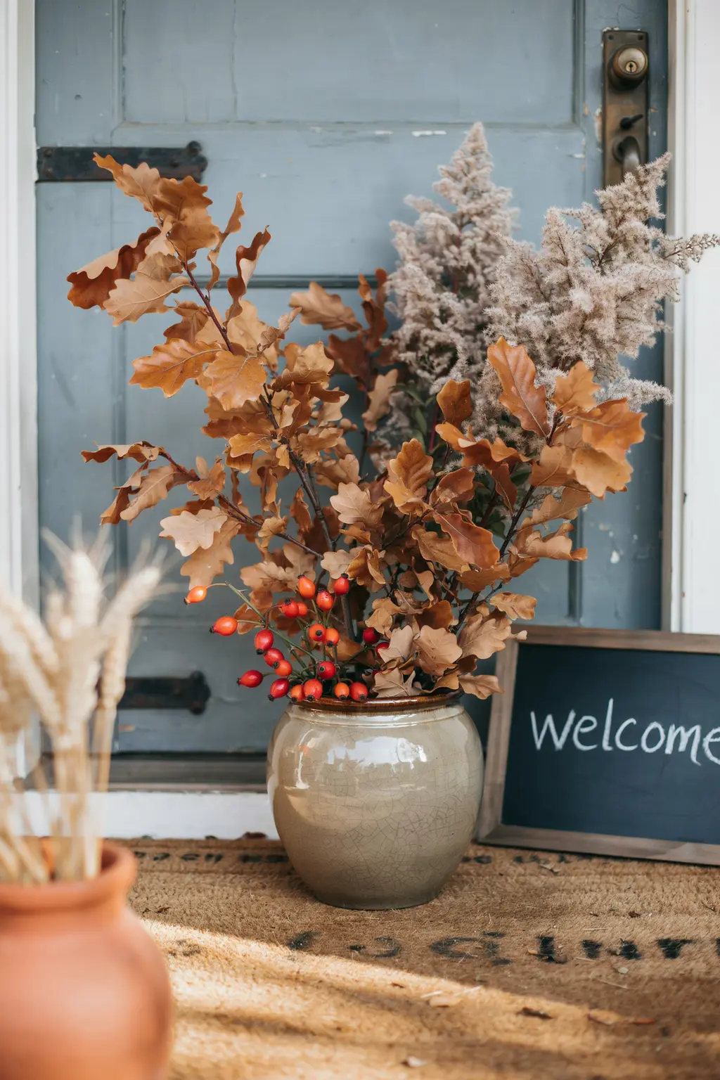 Fall wedding flowers on a budget: turned oak branches, smokebush and rose hips in a stoneware crock by a door