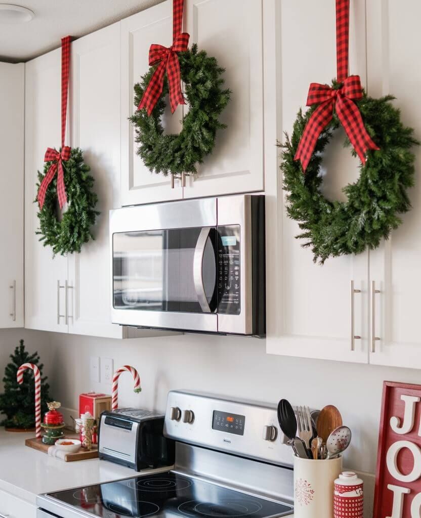 White kitchen cabinets decorated with Christmas wreaths and red plaid ribbons for a festive holiday look.
