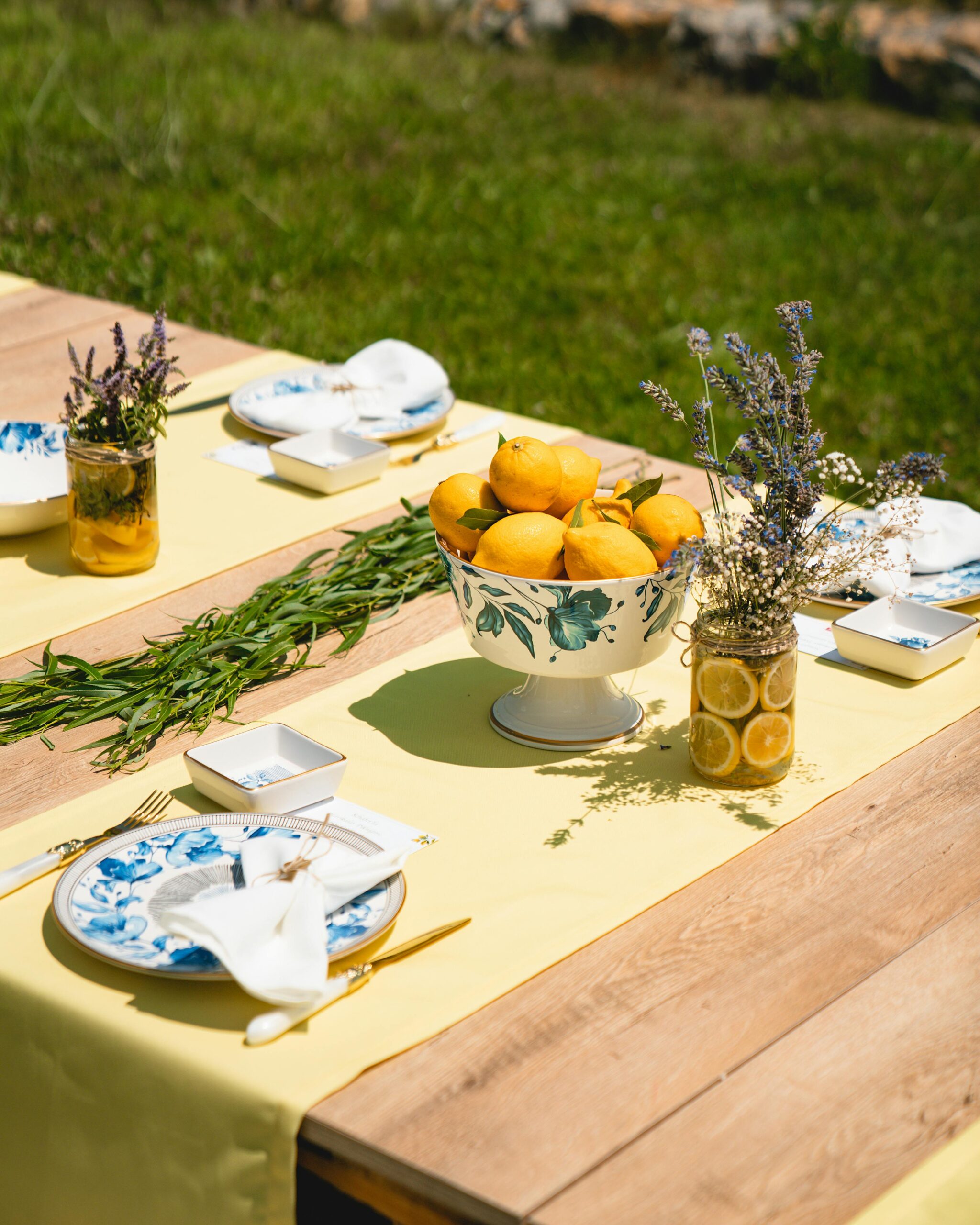 Outdoor lemon table decor and tablescape with yellow tablecloth, lemons in a bowl, lavender and blue-white plates