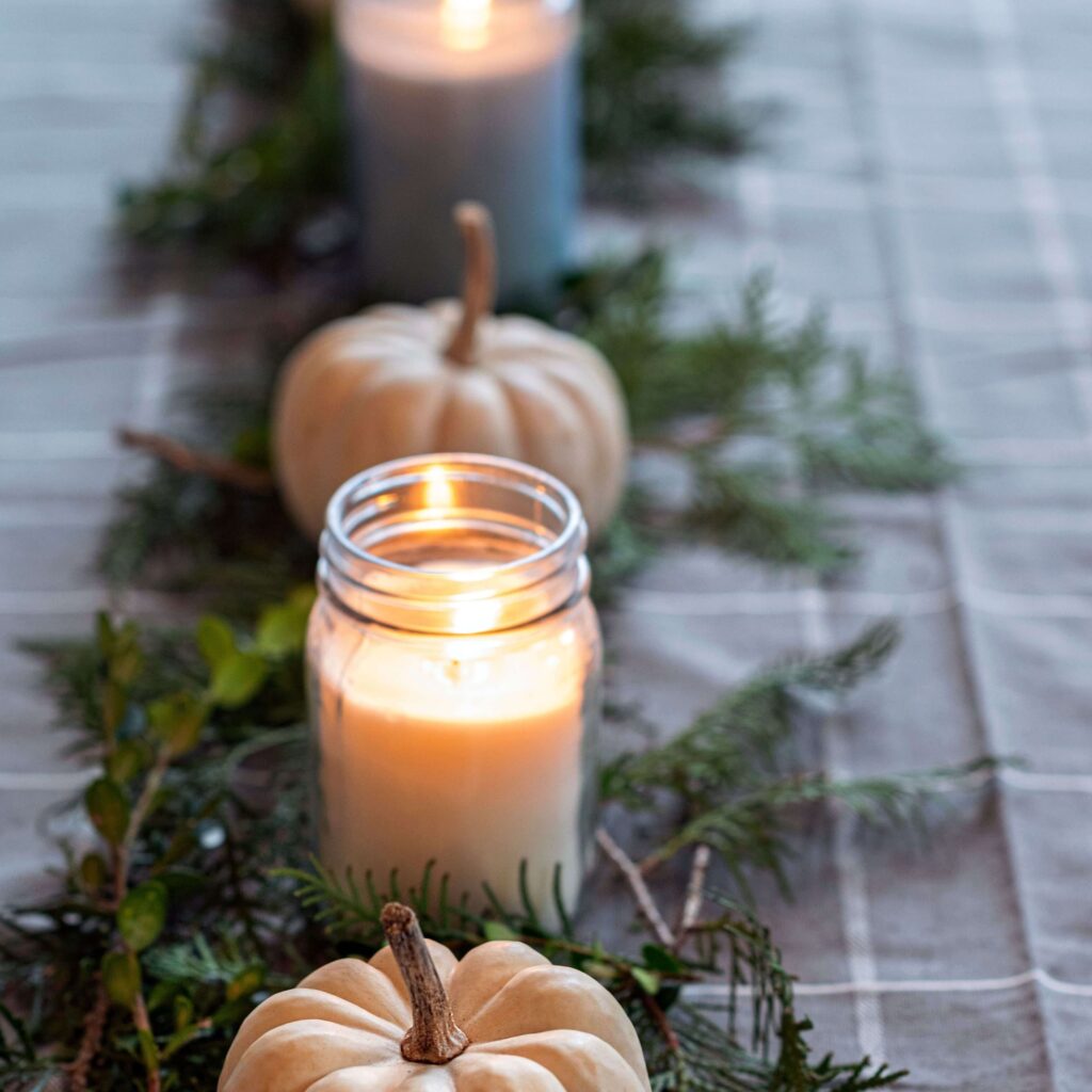 Rustic fall centerpiece with white pumpkins, mason jar candles, and greenery on a plaid tablecloth.