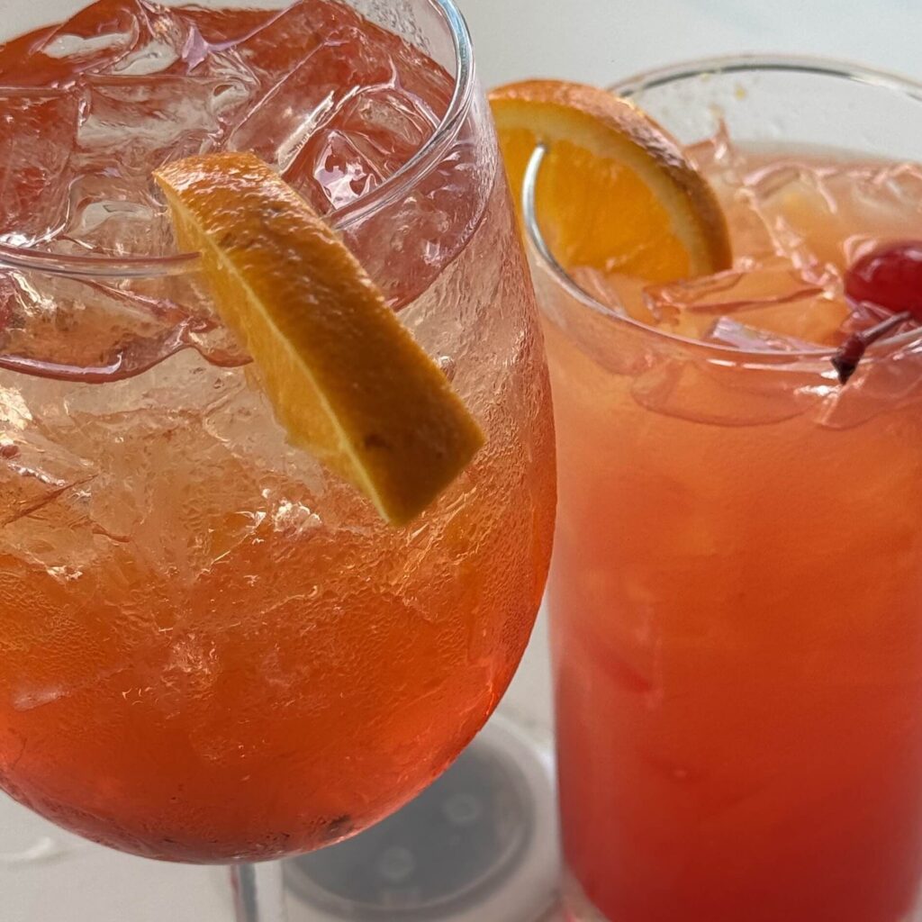 Glasses of Tart Cherry Cinnamon Mocktail with ice, orange slices, and a cherry garnish — a cozy, festive winter drink perfect for slow evenings.